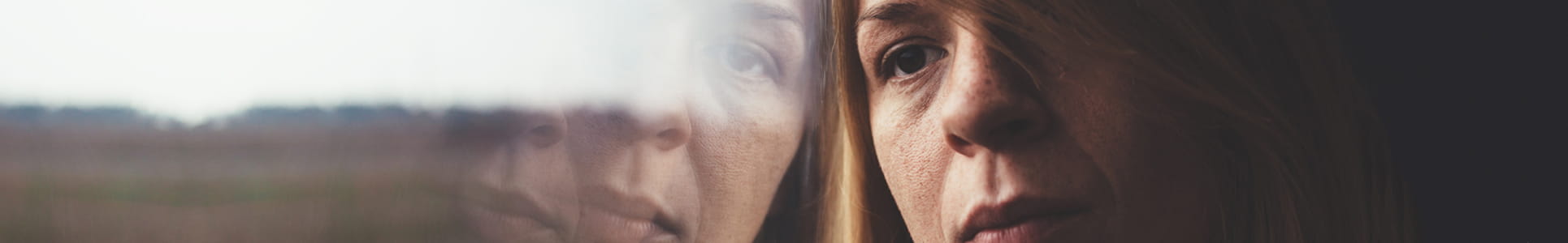 Woman in train alone and sad, reflection of her face in the window